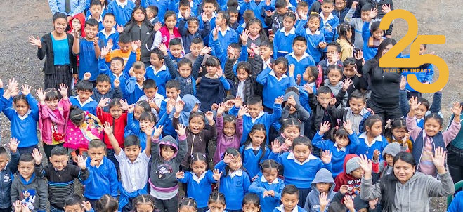 Crowd of children and teachers looking up and waving. 25 Years of Impact logo in top right corner.