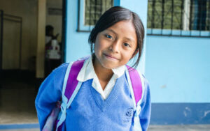 Smiling girl wearing a Vida School blue sweater and a backpack