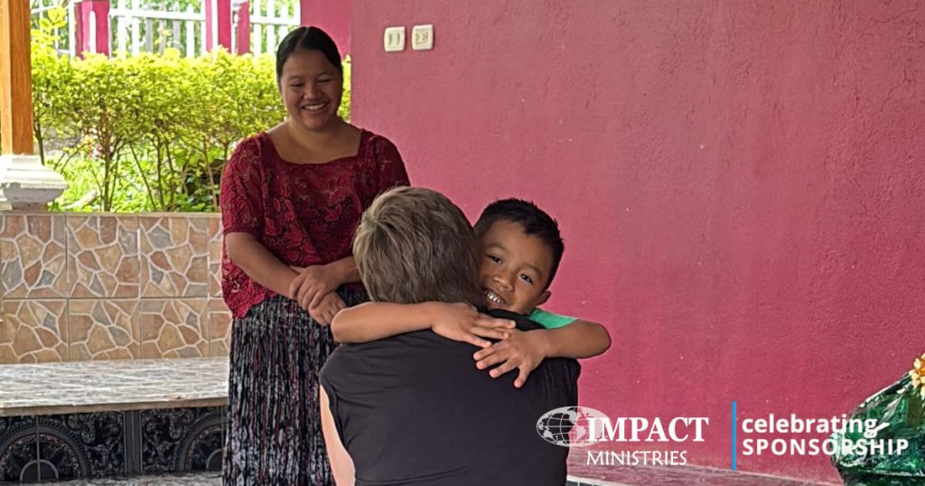 child getting a hug from their sponsor while the mother looks on with a smile